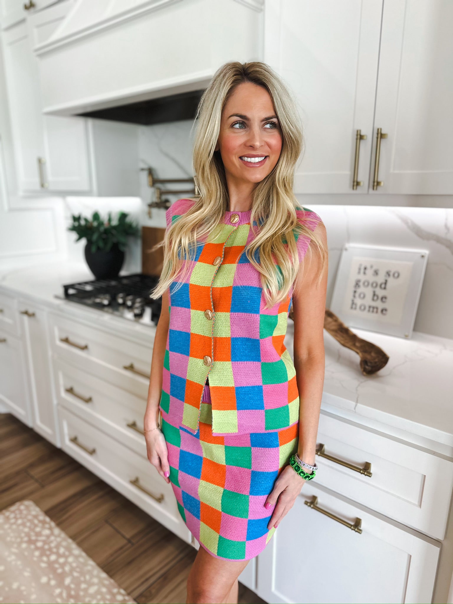 Woman wearing a multicolor checker knit tank top and midi skirt set with gold buttons. Bright pink, orange, blue, and green