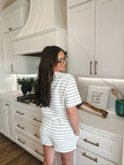 Woman wearing a white and sage green striped loungewear set with shorts and a short-sleeved top. The set is textured and