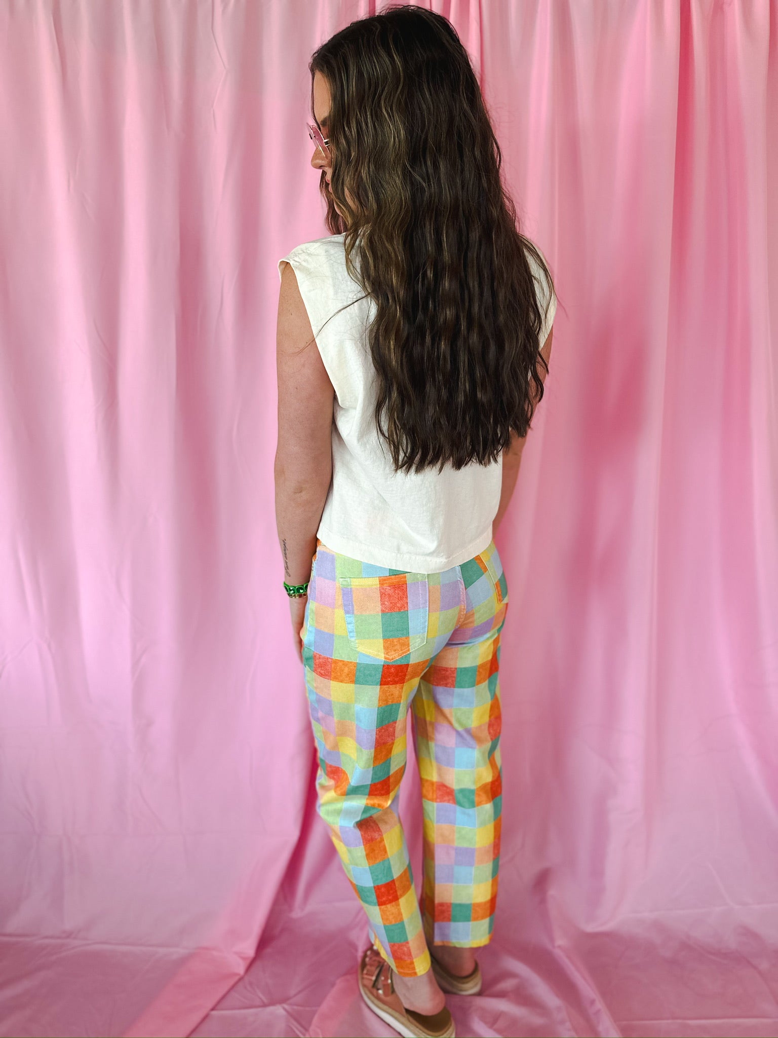 Back view of model wearing vibrant Madras Plaid high waist barrel pants in poppy, pine, yellow, orange, blue stretch denim.