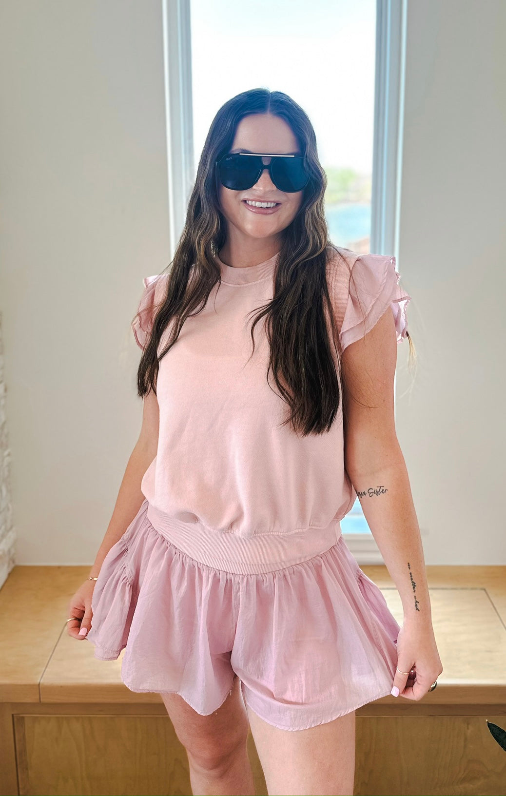Light pink athleisure set featuring a ruffled sleeve pullover and crinkle nylon shorts on a woman wearing sunglasses.