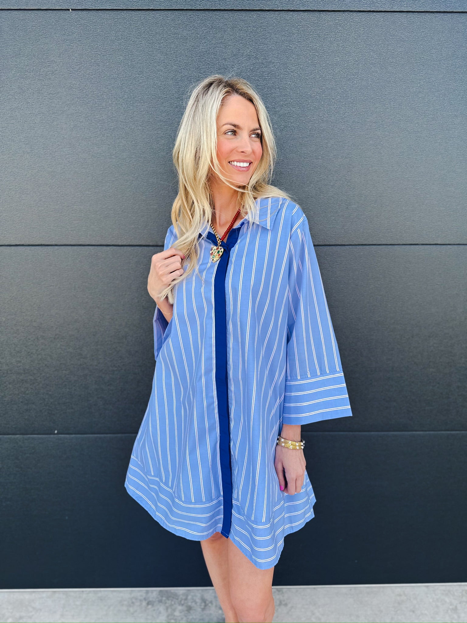 Woman wearing an Entro blue and white vertical striped button up shirt dress with wide sleeves and a dark blue placket.