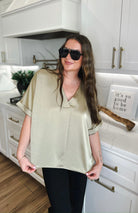 Taupe satin V-neck blouse with cuffed short sleeves, shown on a woman in a modern kitchen.