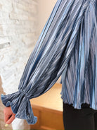Close-up of a slate blue long sleeve top with vertical pleats and ruffled cuffs.