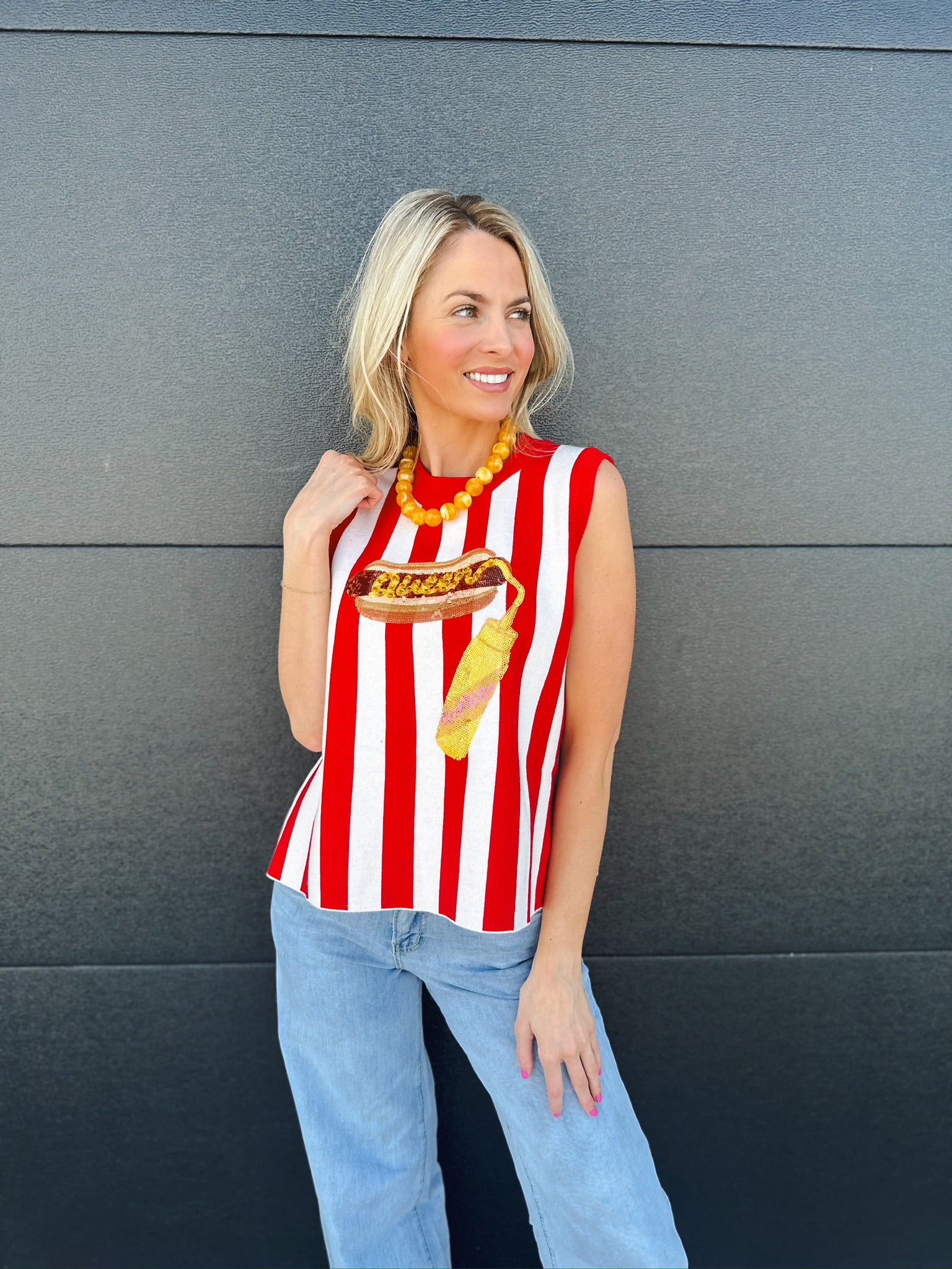 Woman wearing a red and white striped knit tank top with a hot dog and mustard graphic, paired with light wash jeans.