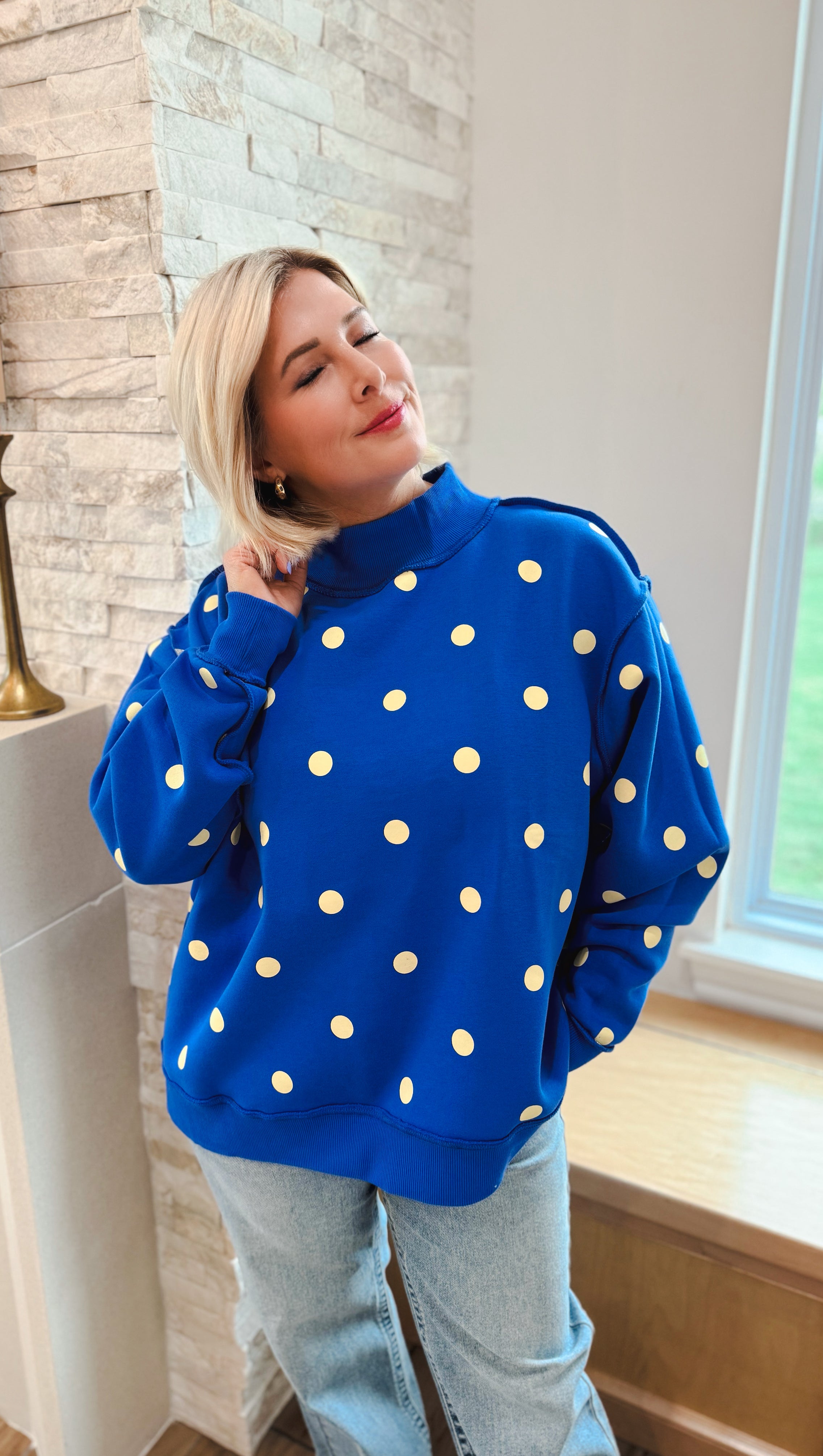 Oversized royal blue sweatshirt with yellow polka dots and a mock neck, worn by a woman with blonde hair.