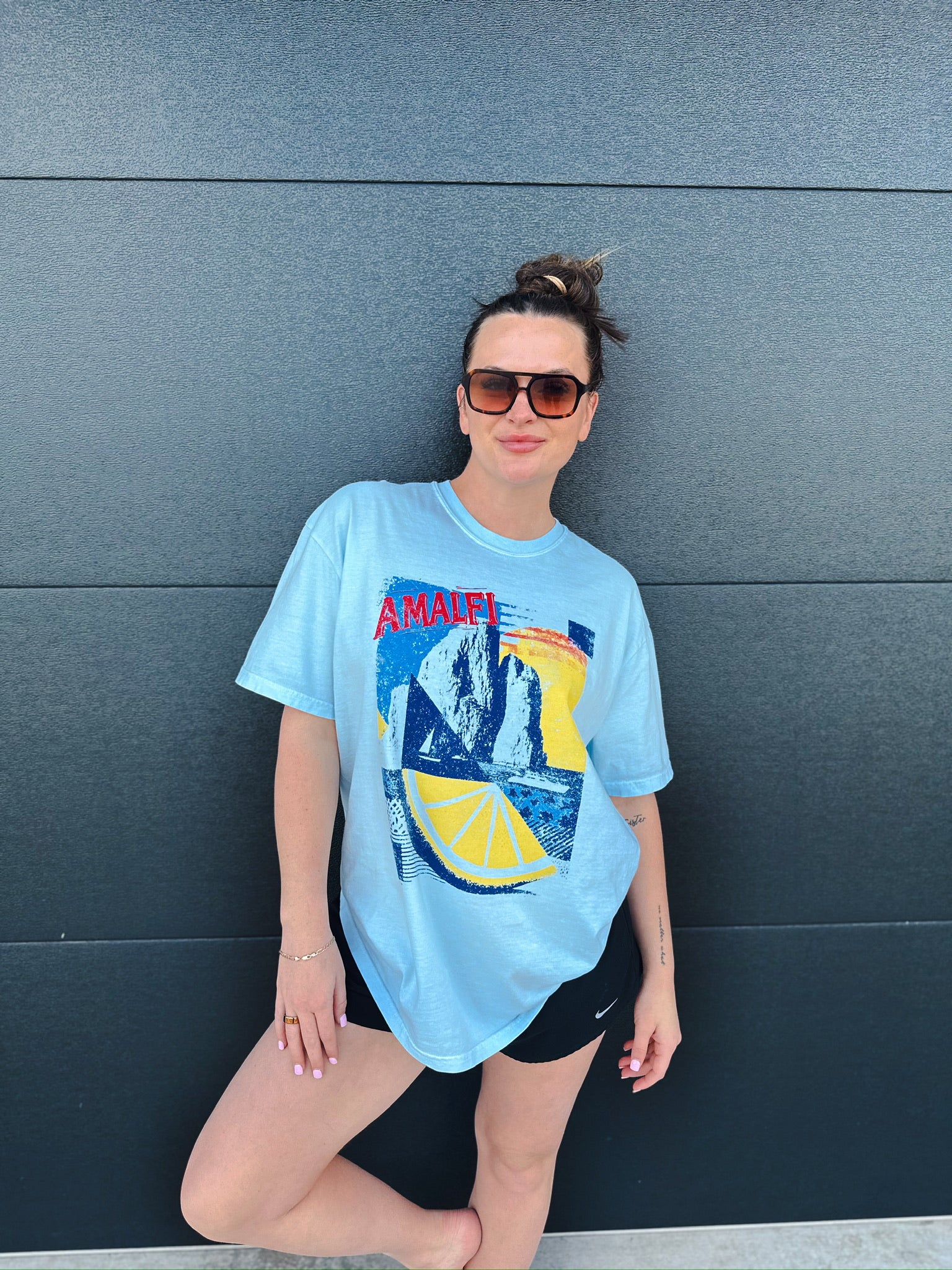 Light blue oversized tee with a vintage Amalfi graphic featuring cliffs, ocean, and a lemon slice. A woman wears it with