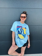 Light blue oversized tee with a vintage Amalfi graphic featuring cliffs, ocean, and a lemon slice. A woman wears it with