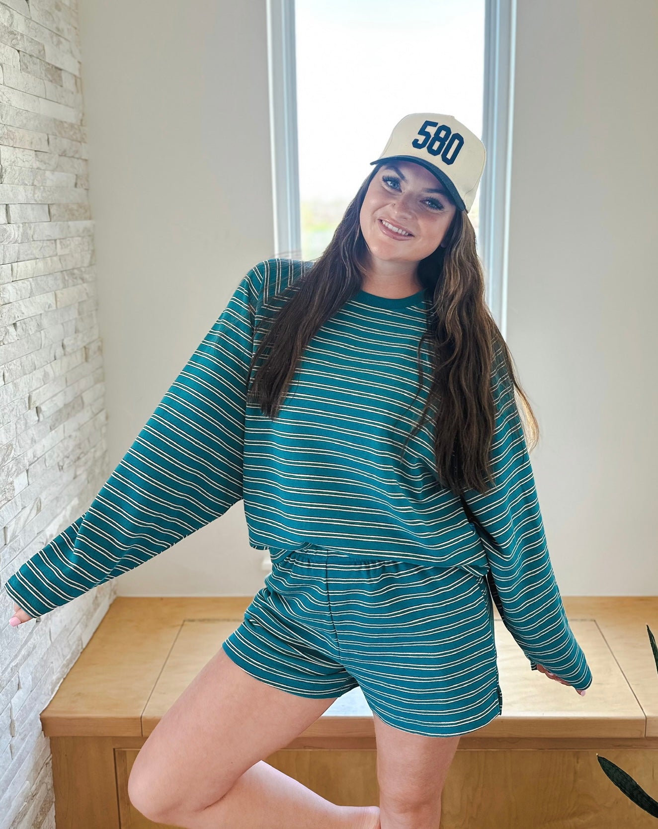 Woman wearing a teal and white striped long-sleeve top and matching elastic waist shorts. She is also wearing a beige