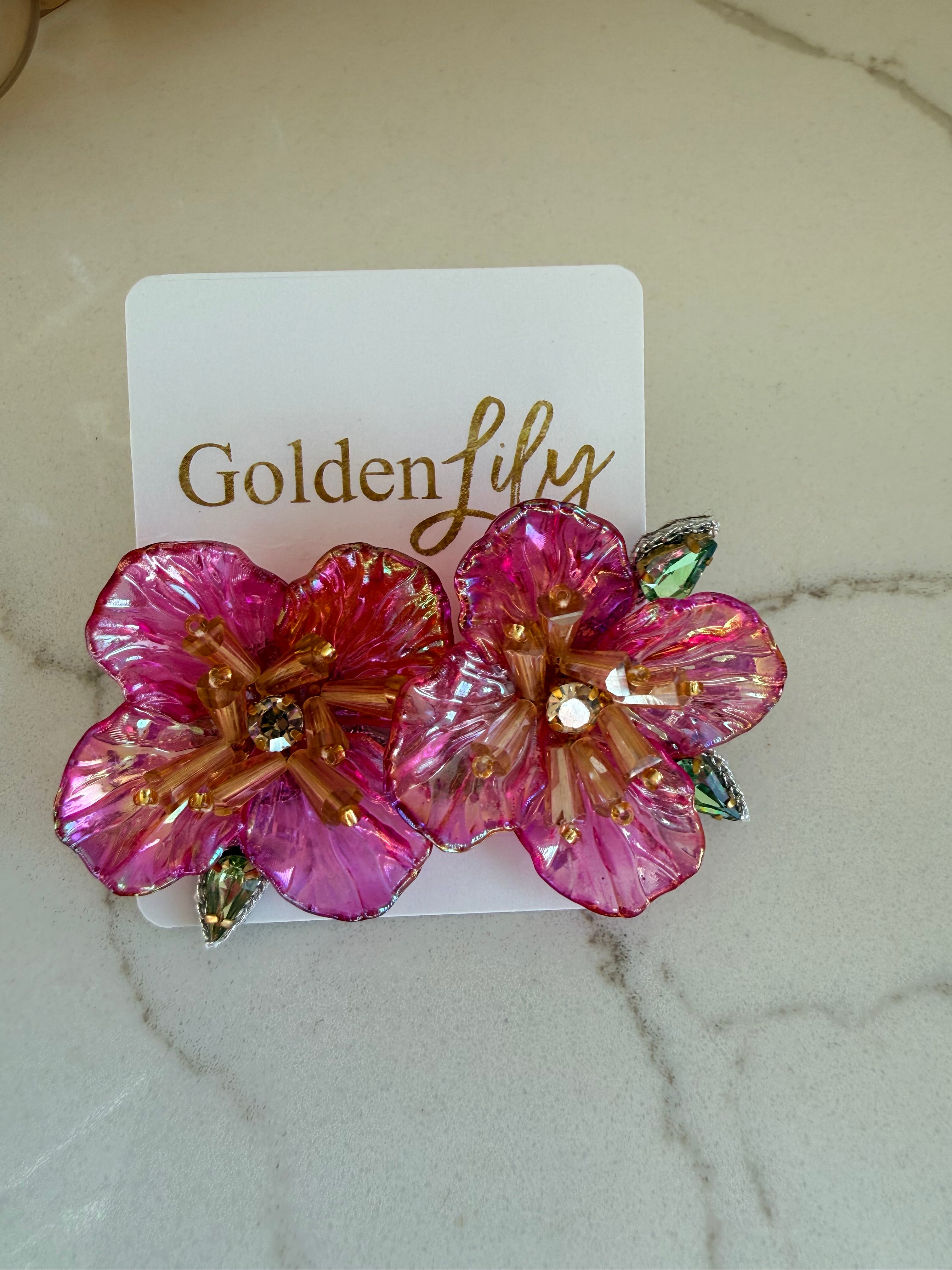 Large pink floral stud earrings with iridescent petals, gold beads, and crystal accents on a white card.