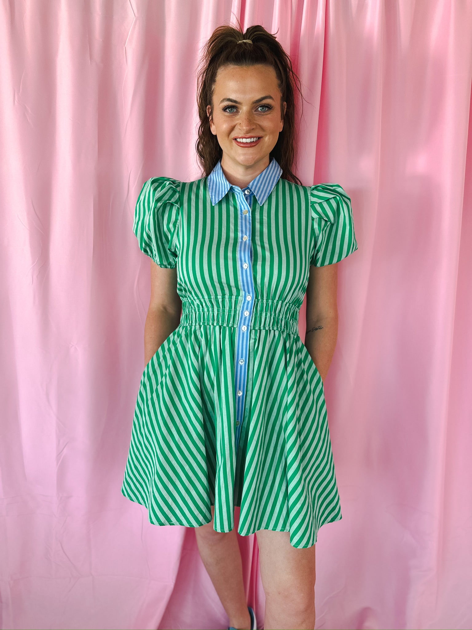 Entro green and white striped mini dress with puff sleeves, blue collar, and shirred waist. Woman smiling against pink