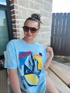 Light blue oversized tee with "AMALFI" graphic print featuring mountains, a sunset, and a lemon slice. Woman wearing