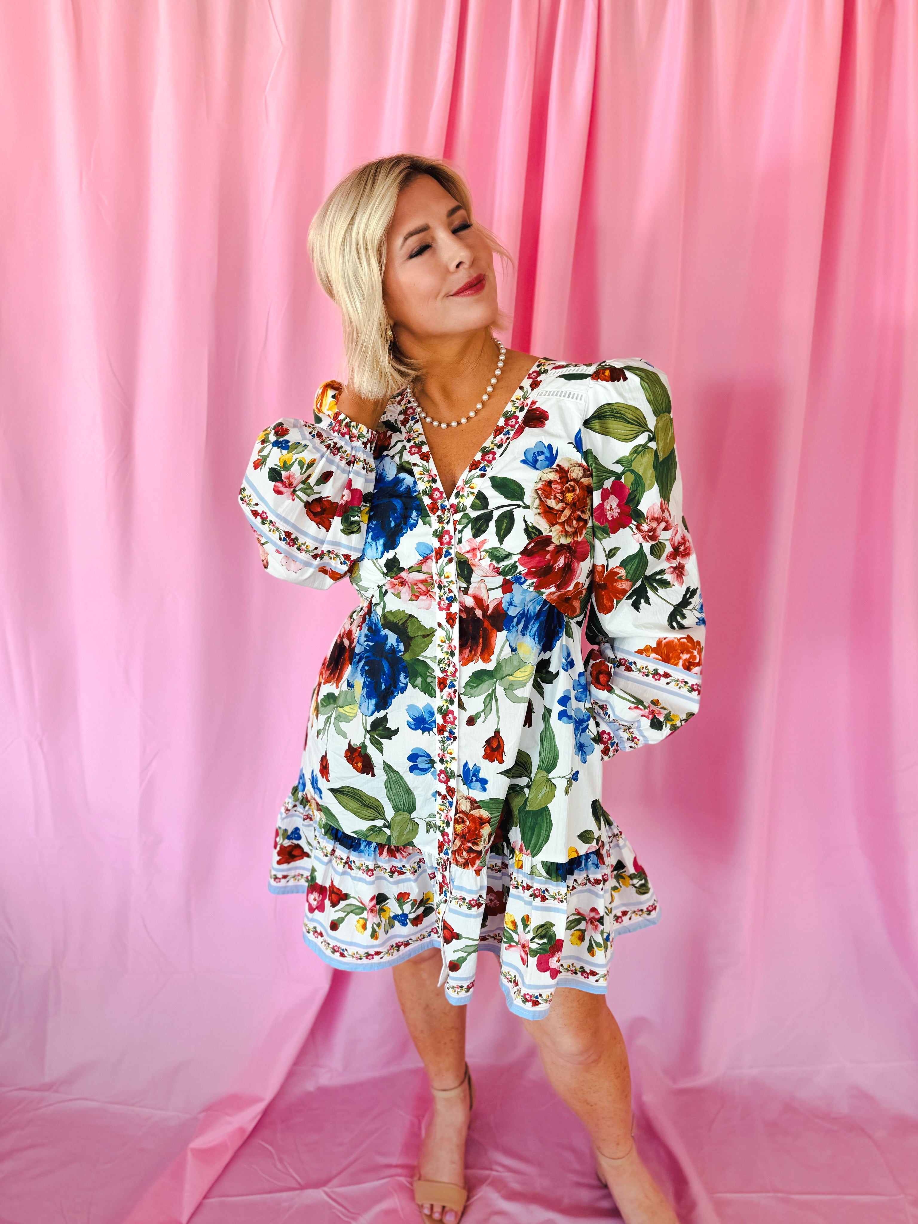 White floral puff sleeve mini dress with V-neck and button front, featuring a vibrant bouquet print and ruffled hem. Model