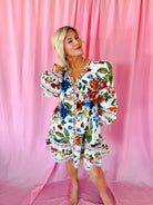White floral puff sleeve mini dress with V-neck and button front, featuring a vibrant bouquet print and ruffled hem. Model