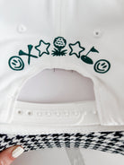 White caddie hat with green embroidered golf-themed icons: smiley face, tee, stars, golf ball on tee, golf flag. Black and