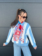 Woman wearing a light blue and white striped sweater featuring a red Queen of Hearts card graphic. She has a red and blue