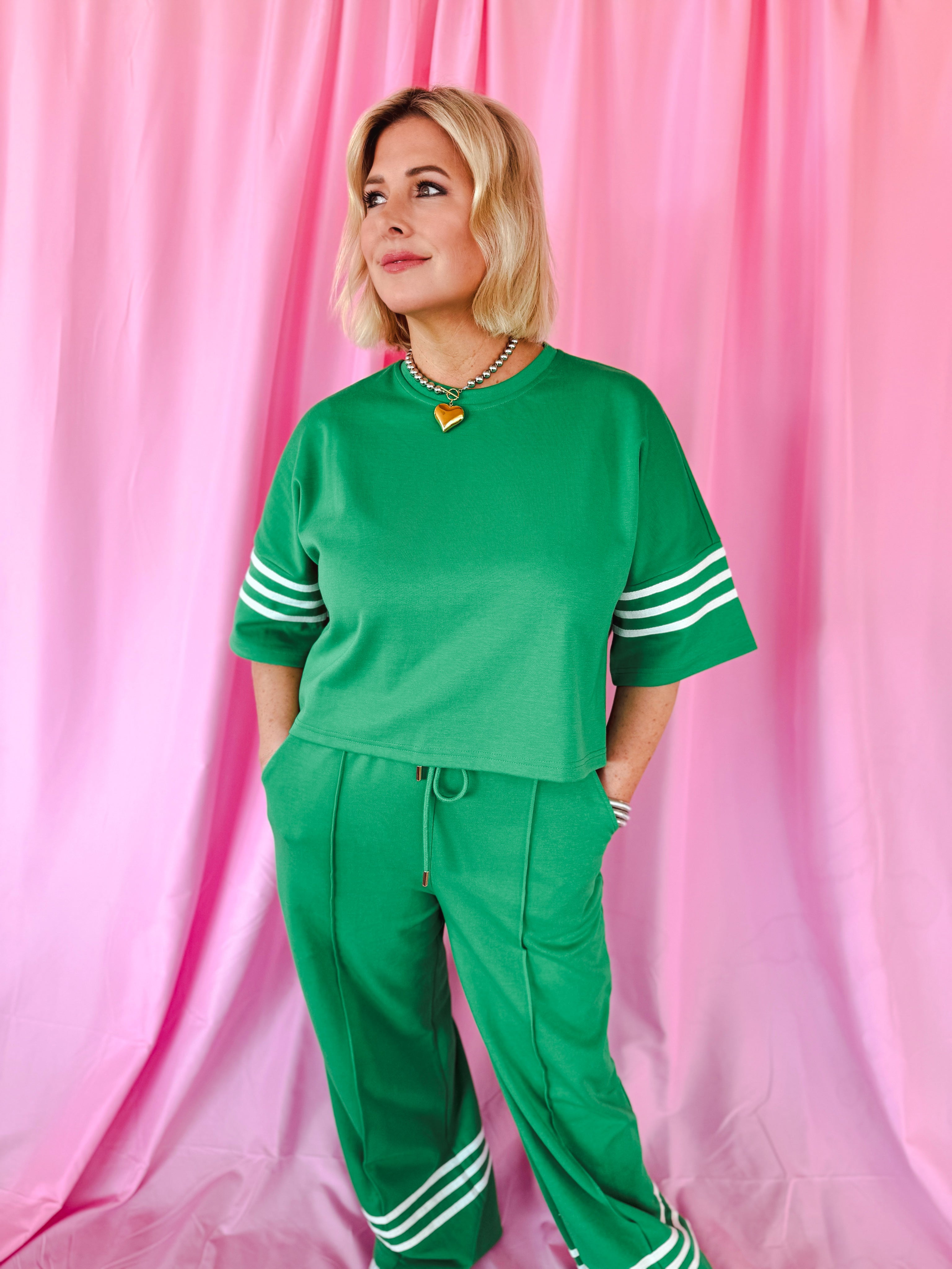 Green Entro matching set with white stripes on sleeves and pants. Woman wearing crop top and wide-leg pants.