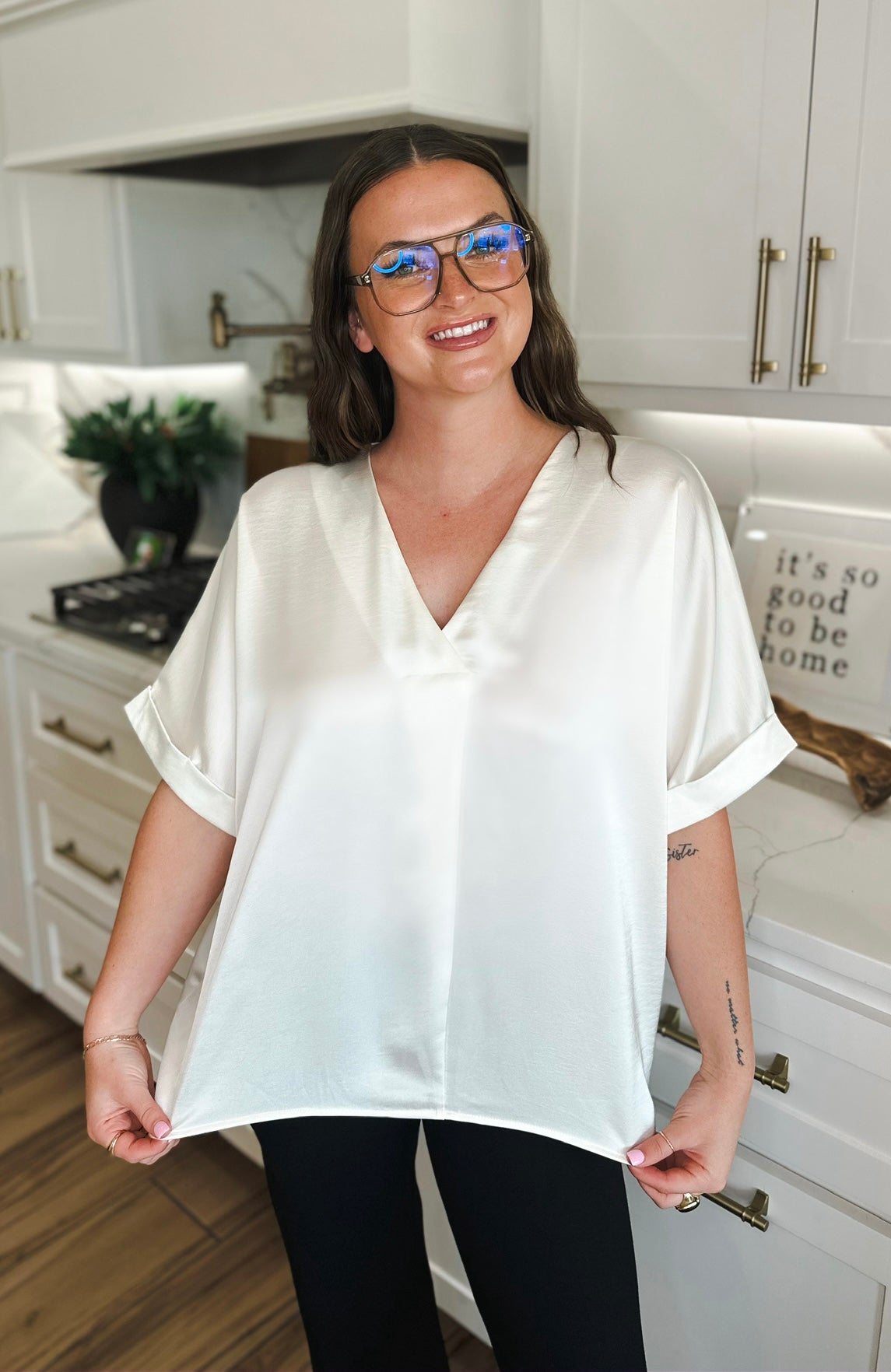 Ivory satin v-neck blouse with folded cuffs on a smiling woman wearing glasses.