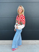 Woman wearing a Queen of Sparkles red and white checkered sequin strawberry cardigan with white sleeves, light wash flare