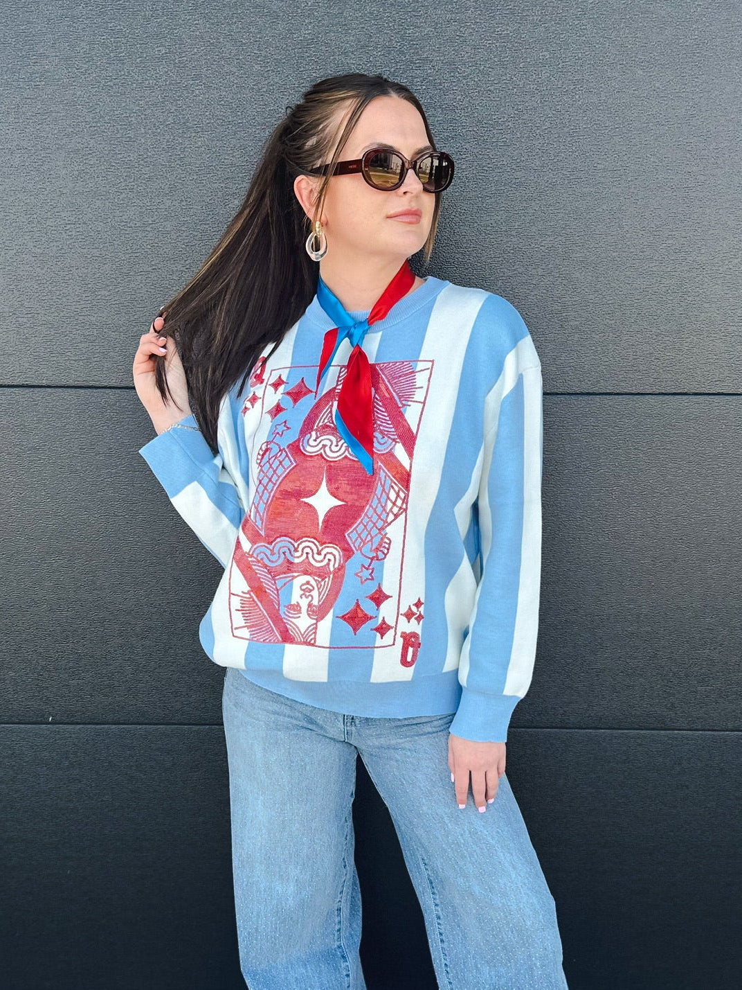 Queen of Sparkles sweater with light blue & white stripes and a red Queen of Hearts card graphic. Model wears jeans & scarf.
