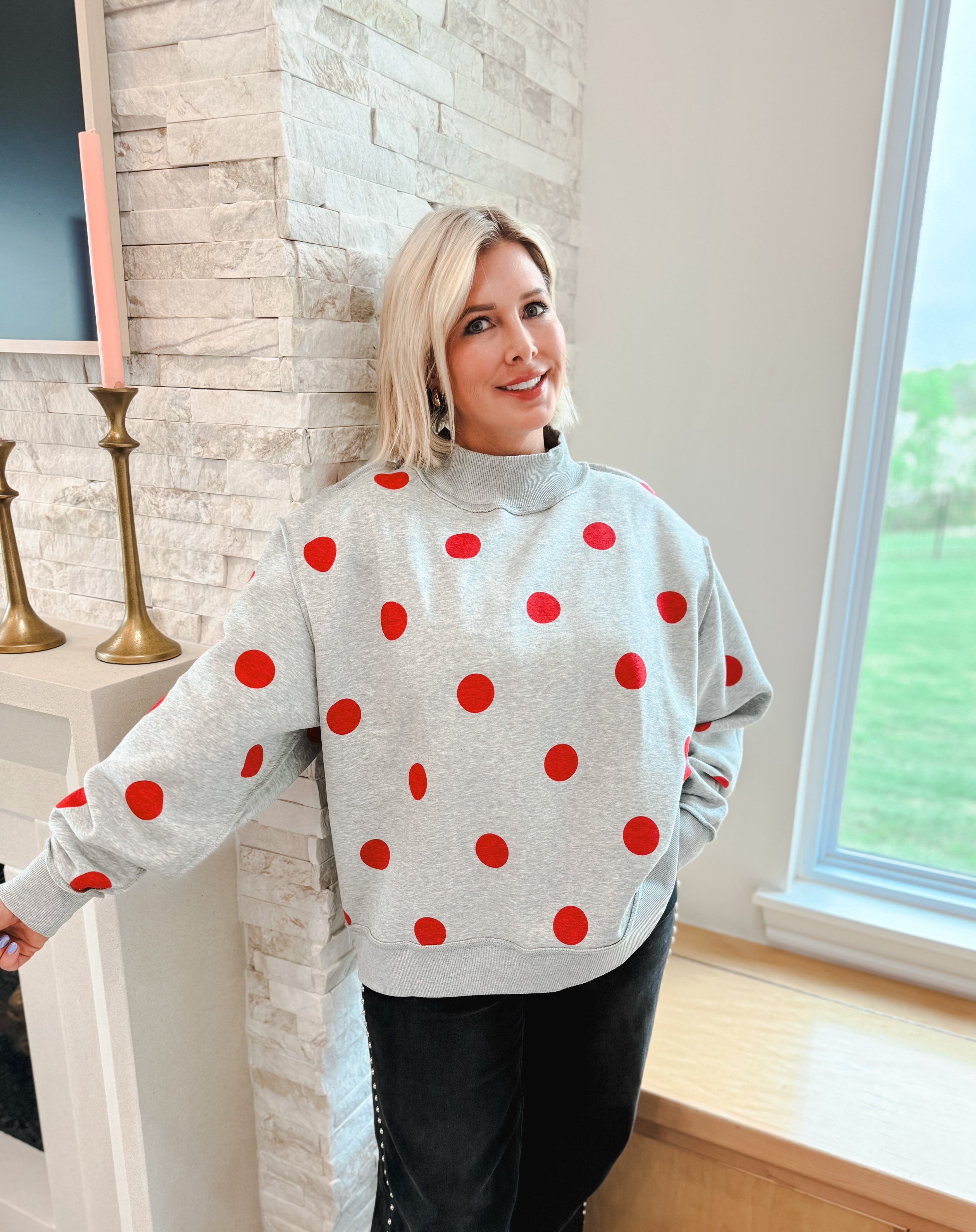 Grey mockneck sweatshirt with red polka dots. Woman wearing oversized sweatshirt and black pants.