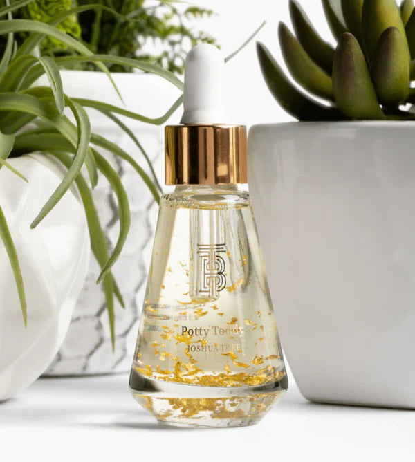 Thomas Blonde Potty Toddy Drops serum bottle with gold flakes, dropper lid, and gold accent. Botanical background.