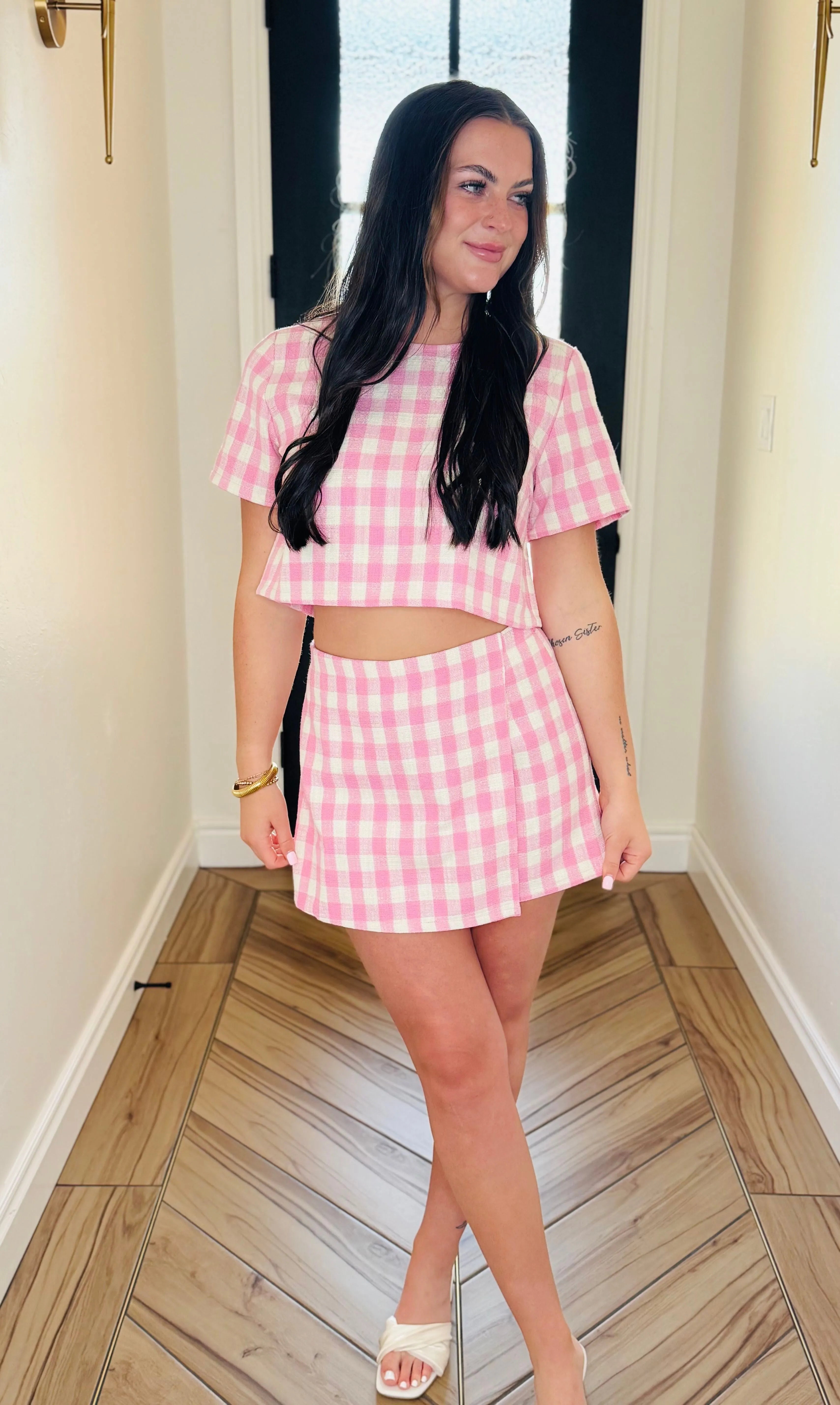 Pink gingham tweed skort set with short sleeves and a mini skirt. Model wears a gold bracelet and white sandals.