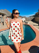 Cream mini dress with large red polka dots, spaghetti straps, and a flared hem, worn by a woman outdoors.