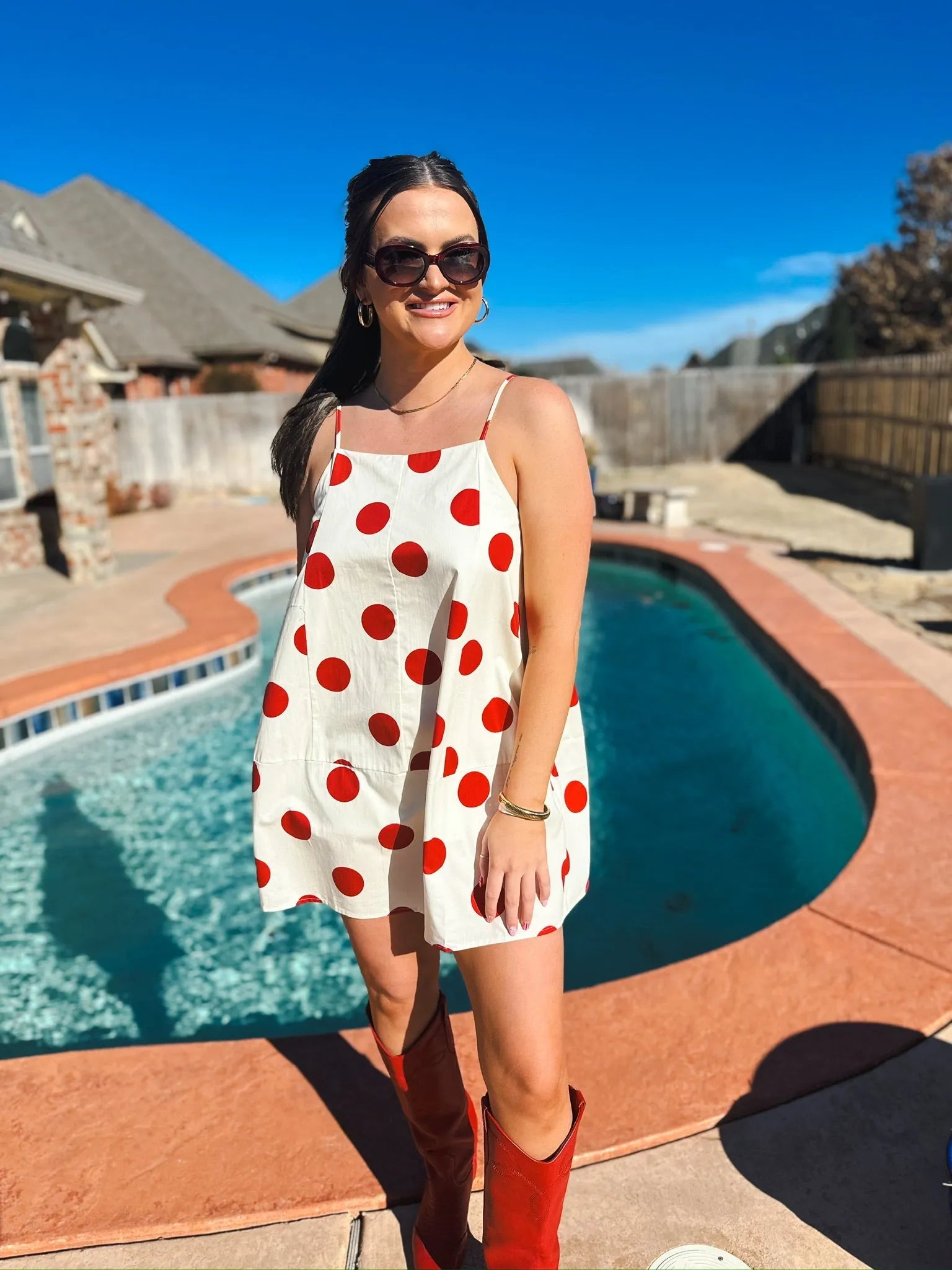 Woman in a cream mini dress with big red polka dots, spaghetti straps, and red cowboy boots.