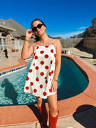 Woman in a red and cream polka dot mini dress with spaghetti straps and red cowboy boots.