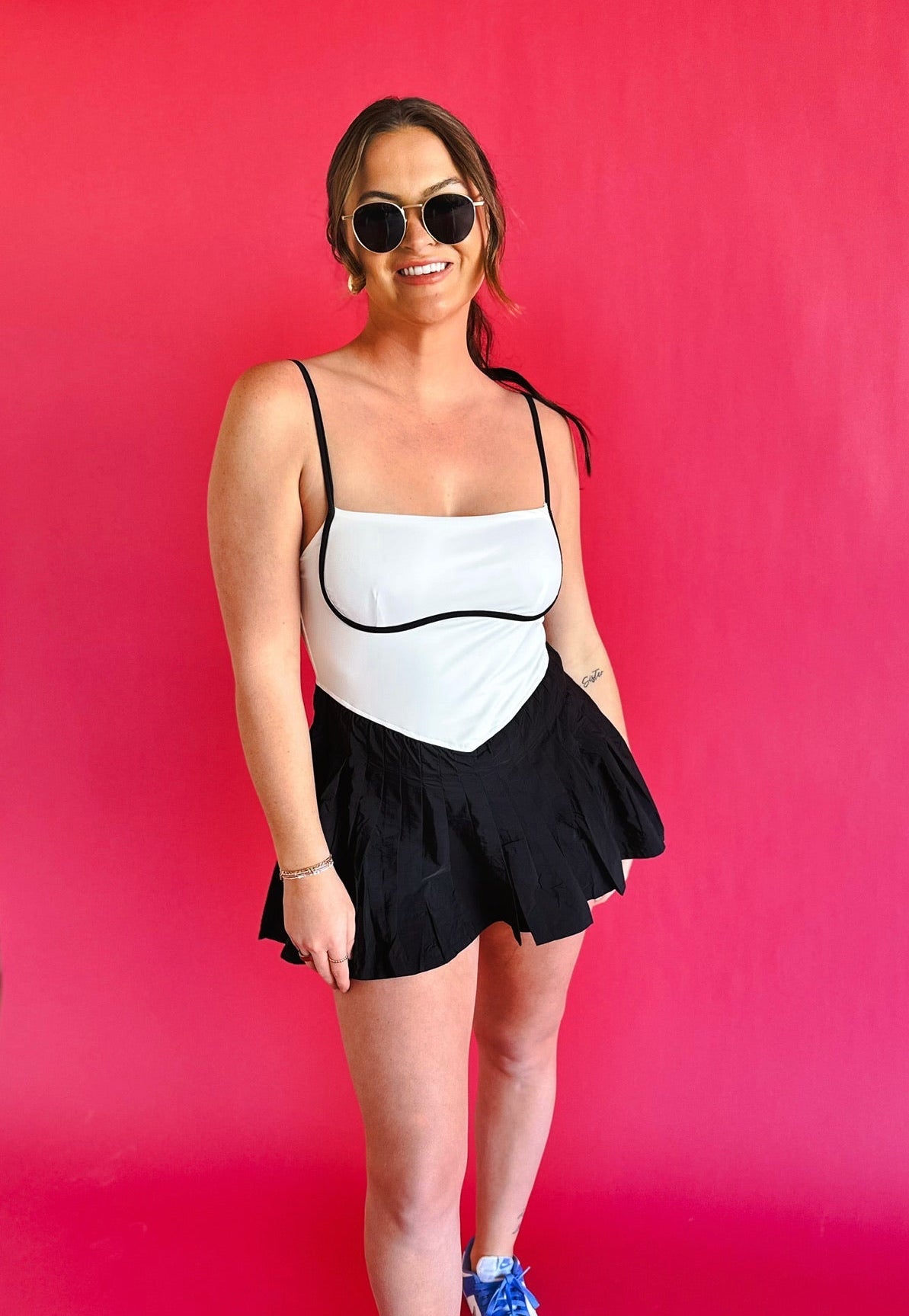 Black & white colorblock athletic dress with spaghetti straps and a pleated skirt. Model wears sunglasses and blue sneakers.