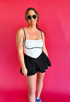 Black & white colorblock athletic dress with spaghetti straps and a pleated skirt. Model wears sunglasses and blue sneakers.