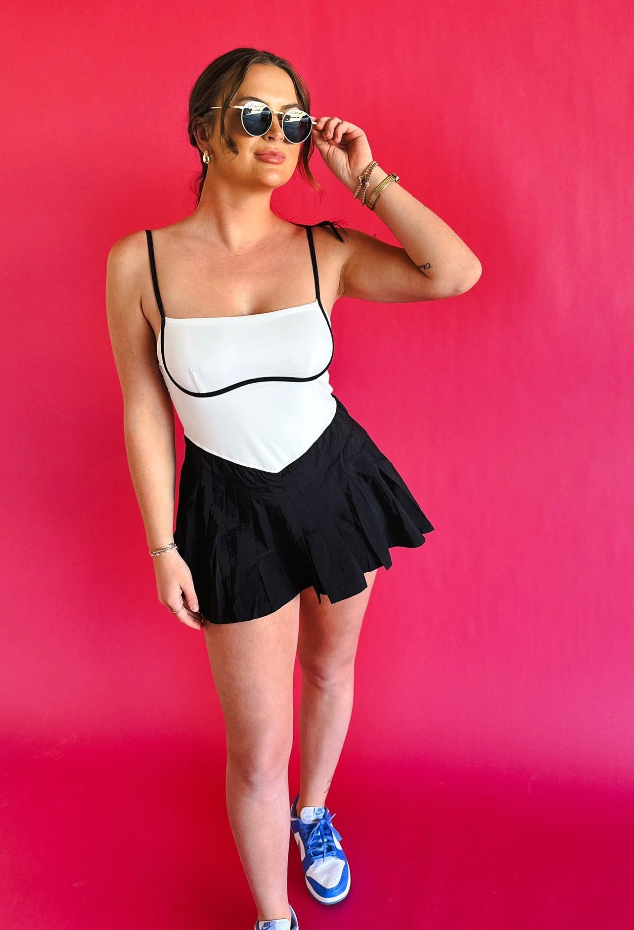 Woman wearing a black and white colorblock athletic dress with spaghetti straps and a pleated black skirt. She has on round