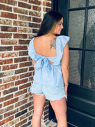 Model wearing the Blue Gingham Bow Tie Back Top with high-rise denim, highlighting the flirty open back and trendy self-tie bow design.