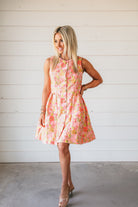 Bright pink brocade dress with vibrant floral print in coral, lime, and yellow. Sleeveless, A-line, button-front design.