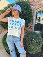 Woman wearing a white casual tank top with blue text "EVERY LITTLE THING is gonna be alright", ripped light wash jeans