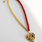 Gold chain necklace with half red beaded strand, featuring a heart pendant with colorful gemstone confetti.