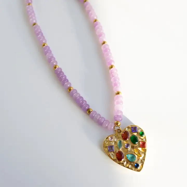 Gold heart pendant necklace with colorful gems, strung on light purple and pink glass beads with gold spacers.