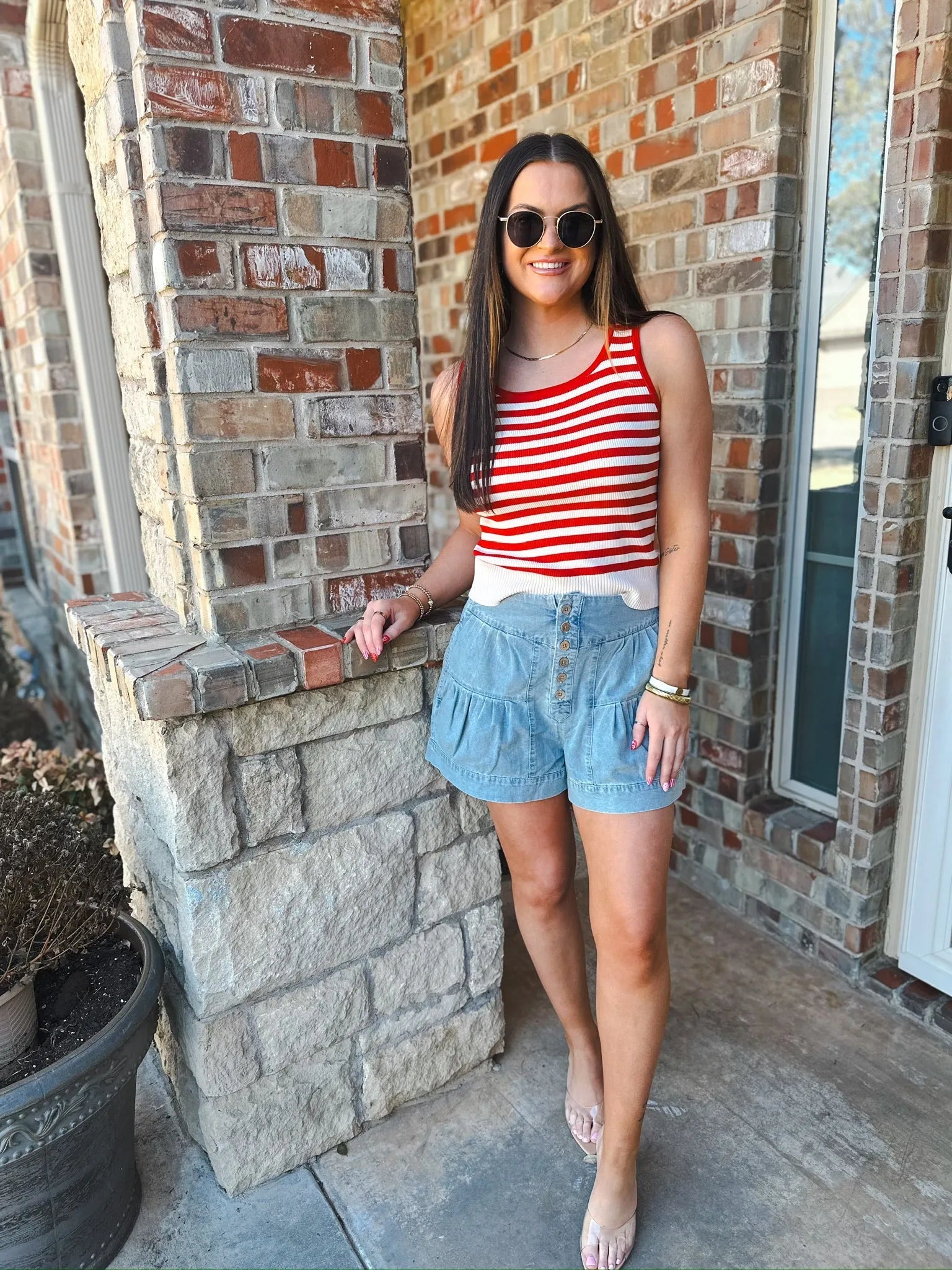 Woman wearing a cream and red striped tank top with a white hem and light blue denim ruffled shorts with a button-up front.