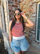 Woman wearing a red and cream striped knit tank top and light wash denim ruffle shorts, accessorized with sunglasses and