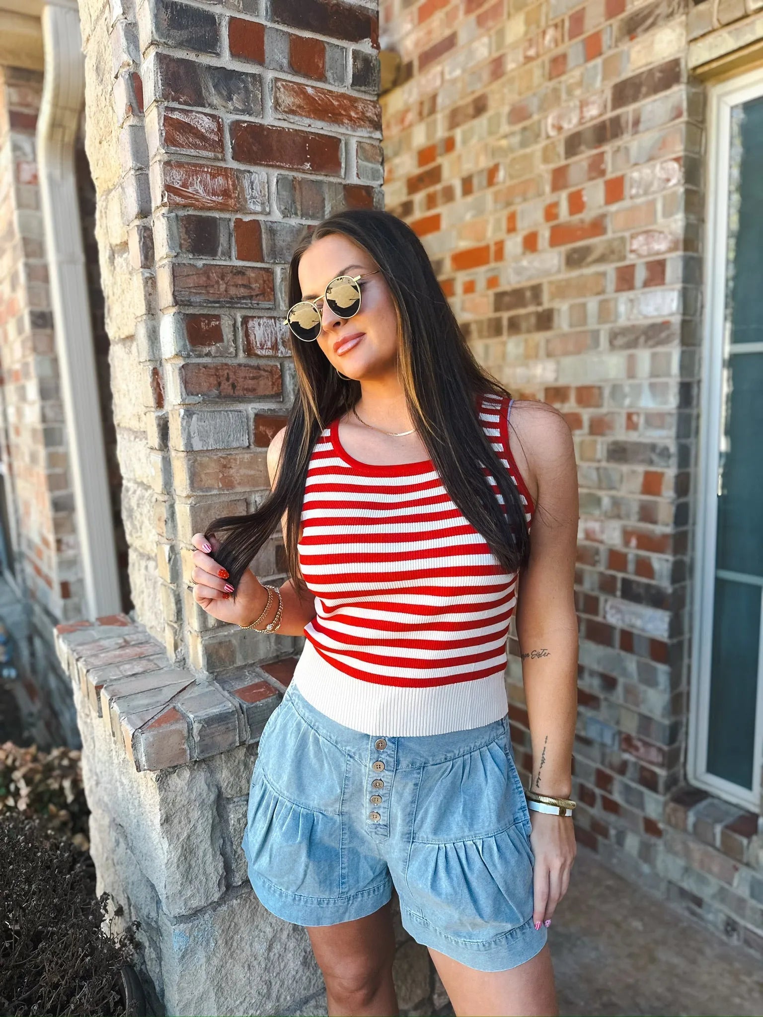 Woman wearing a red and white striped ribbed tank top and light blue ruffled button-front shorts, accessorized with