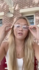 Oversized clear lens DAX blue light blocking glasses with gold frames. Woman with blonde hair adjusts frames.