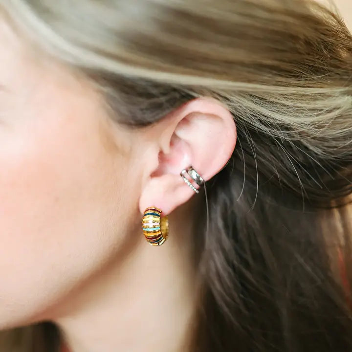 Close-up of a person's ear featuring a colorful, striped 18K gold-plated hoop earring and two silver ear cuffs.