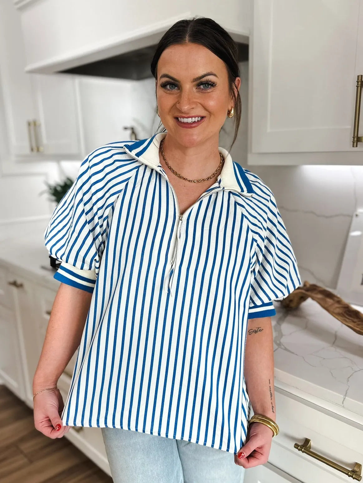 Woman wearing a blue and white striped zip V-neck top with short puffy sleeves and a white collar.