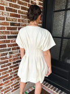 Cream dress with deep V neck, short sleeves, and pleated details on back. Pockets are implied.