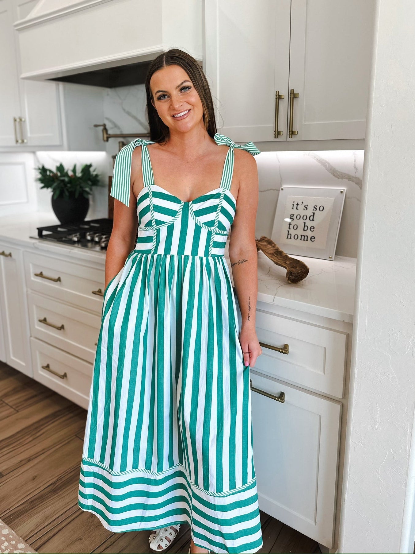 Woman wearing a green and white striped midi dress with tie straps and pockets, standing in a kitchen.