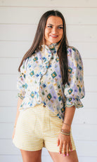 Light purple floral embroidered blouse with ruffle trim and puff sleeves, paired with yellow gingham shorts.