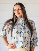 Woman wearing a light purple blouse with a patchwork-like floral print, ruffle collar, and ruffled cuffs. High neck