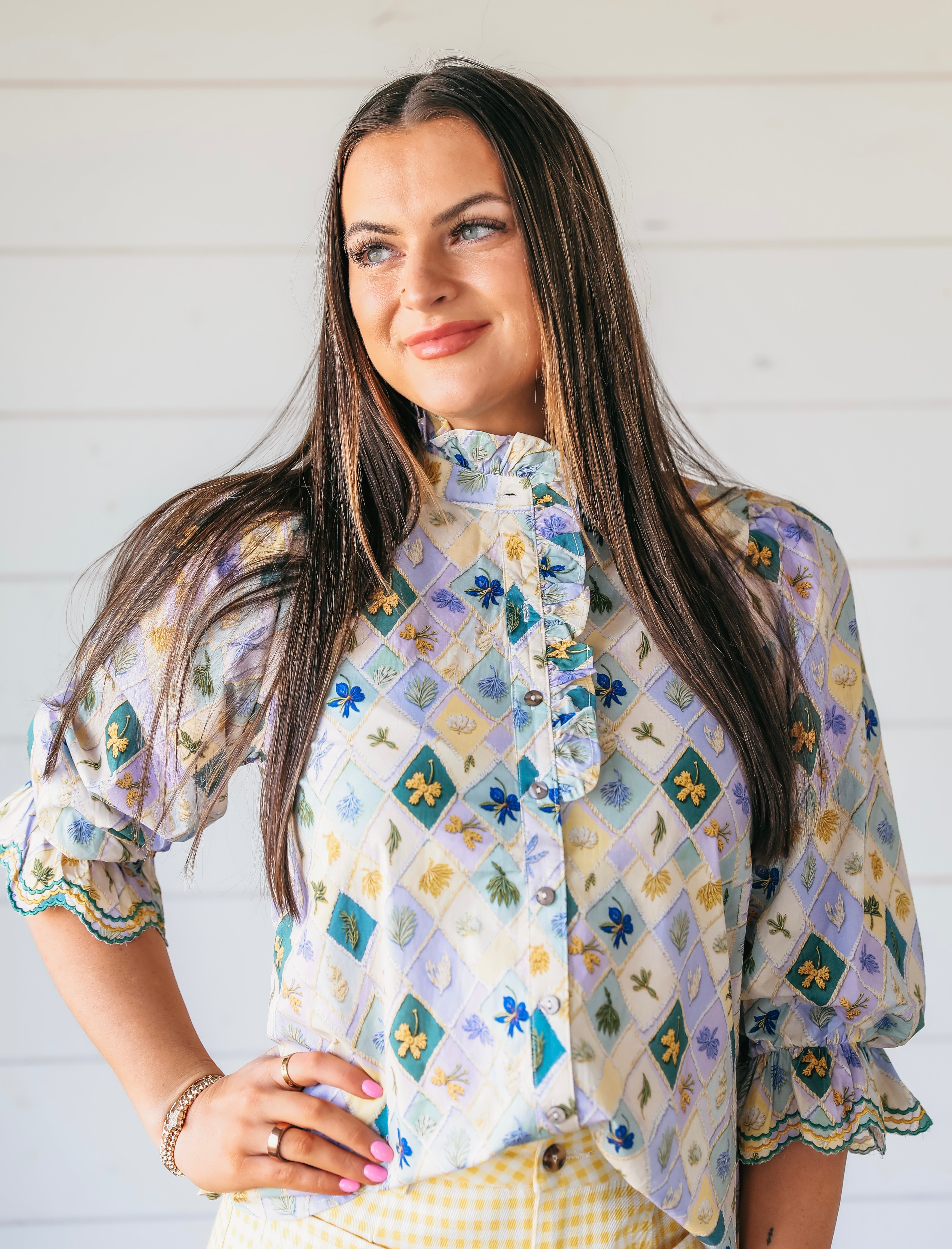 Woman wearing a light purple blouse with a patchwork-like floral print, ruffle collar, and ruffled cuffs. High neck