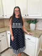 Entro navy blue sleeveless midi dress with white eyelet floral embroidery and tiered bodice. Woman wearing glasses and