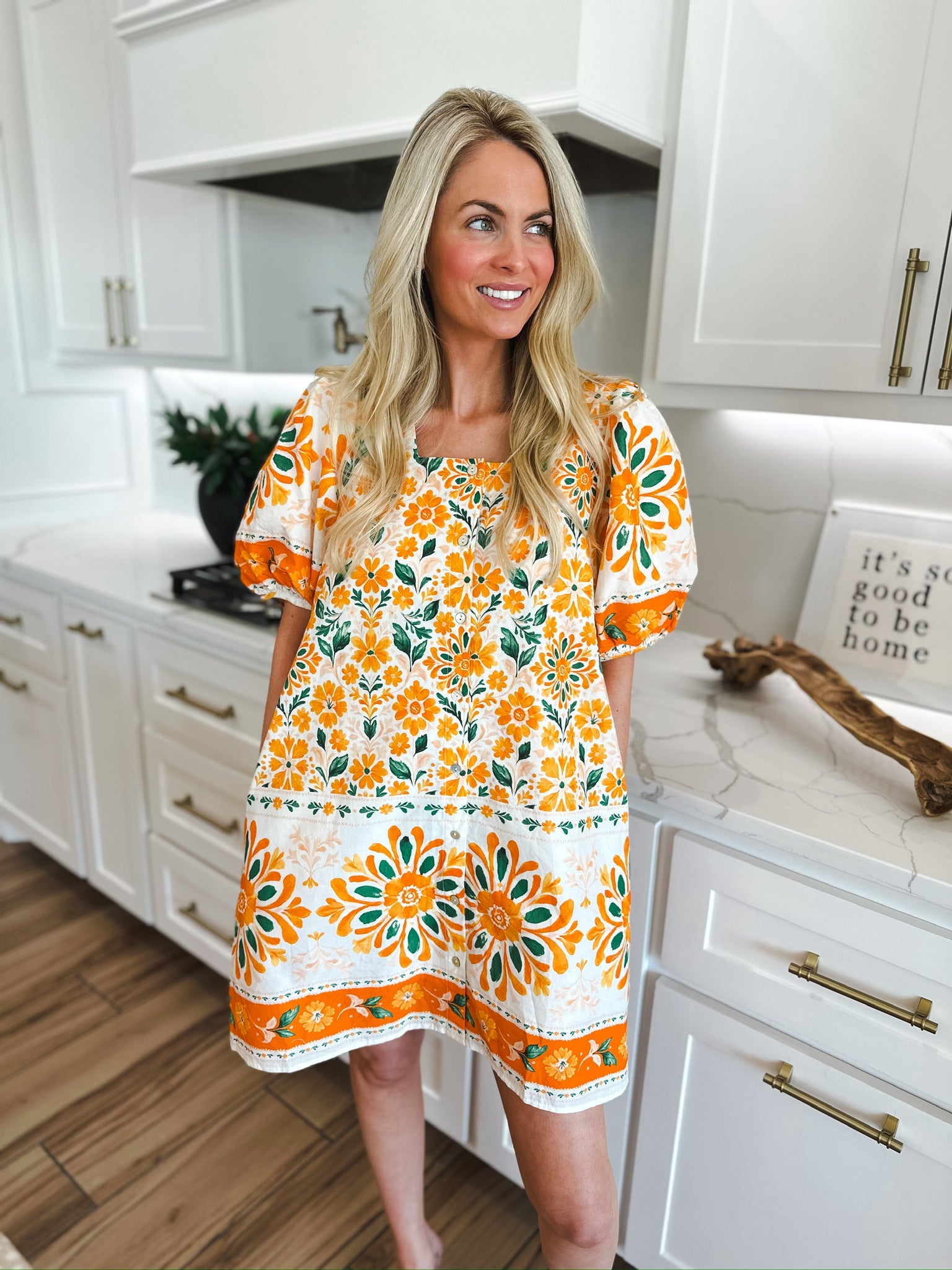 Entro orange floral puff sleeve mini dress with white and green accents. Woman wearing the dress in a kitchen.